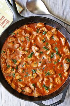 a skillet filled with chicken and sauce on top of a wooden table