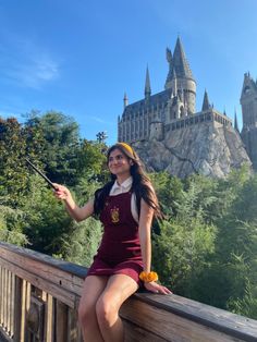 a young woman sitting on top of a wooden fence next to a hogwarts castle