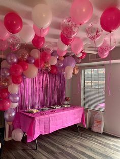 pink and white balloons are hanging from the ceiling above a table with a cake on it