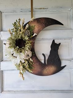 a metal cat sitting on top of a moon with flowers hanging from it's side