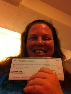 a woman holding up a cheque in front of her face and smiling at the camera