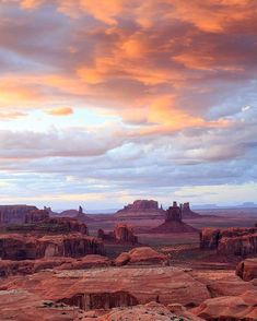 the desert is full of rock formations under a colorful sky with clouds in the distance