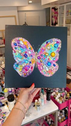 a person holding up a butterfly made out of buttons and other crafting supplies on a table