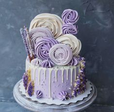 a cake decorated with purple icing and flowers on a table next to a gray wall