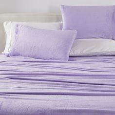 a bed covered in purple sheets and pillows