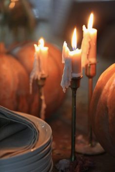 three lit candles sitting on top of plates next to pumpkins