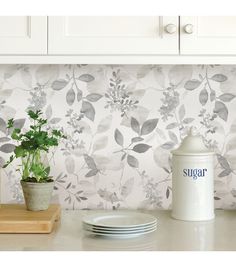 a kitchen counter with plates and cups on it, next to a wallpapered backsplash