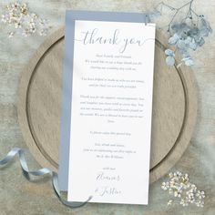 a thank card on a wooden plate with flowers and blue ribbon around the edge that says, thank you