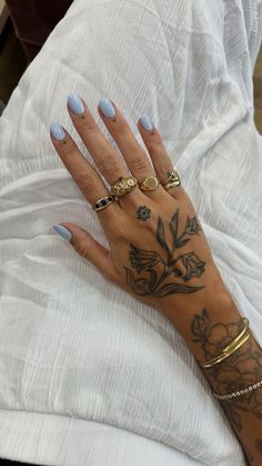 a woman's hand with tattoos and rings on her left arm, sitting on a bed