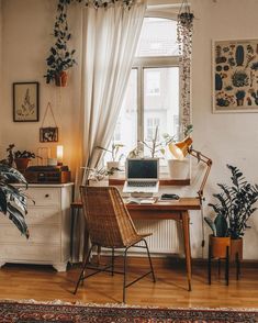 a desk with a laptop on top of it in front of a window filled with potted plants