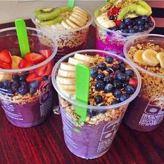 three plastic cups filled with different types of fruit and cereal on top of a wooden table