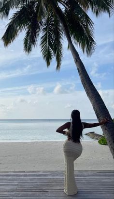 a woman standing under a palm tree on the beach