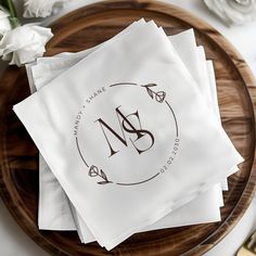 napkins with monogrammed initials on them sitting on a wooden plate next to flowers