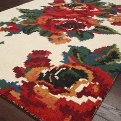 a white rug with red and green flowers on it sitting on a wooden floor next to a hardwood floor