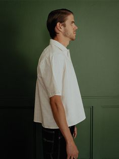 a man standing in front of a green wall wearing a white shirt and black pants