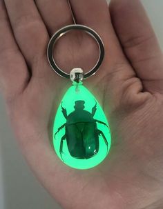 a hand holding a keychain with a green light up beetle in the shape of a man's head