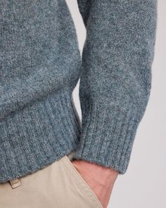 a close up of a person's hand wearing a blue sweater and khaki pants