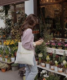 a woman is looking at flowers in a flower shop while holding a tote bag