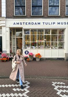 a woman walking down the street in front of a flower shop