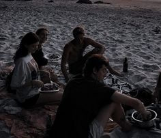 a group of people sitting on top of a beach next to the ocean at sunset