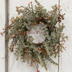 a wreath hanging on the side of a white door with red berries and green leaves