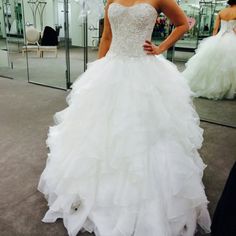 a woman standing in front of a mirror wearing a wedding dress with ruffles