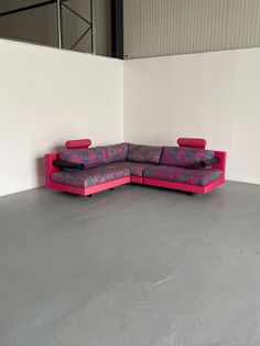 a pink couch sitting on top of a cement floor next to a white wall in an empty room