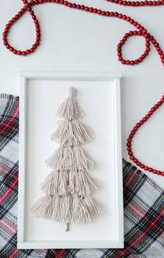 a christmas tree made out of yarn in a white frame on a plaid tablecloth