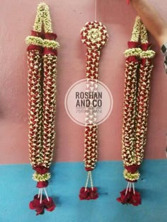 three red and gold beaded items hanging on a pink wall next to each other