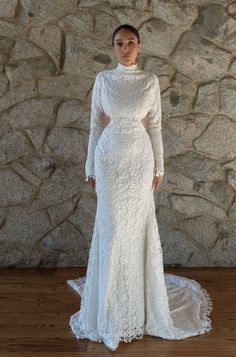 a woman standing in front of a stone wall wearing a white dress with long sleeves