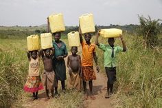 some people are standing on a dirt road and holding large yellow containers over their heads