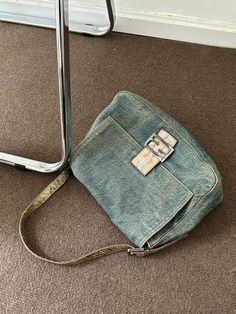 an old purse sitting on the floor next to a metal stand with a cell phone in it