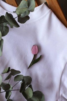 a white shirt with a pink flower pinned to the chest and green leaves around it