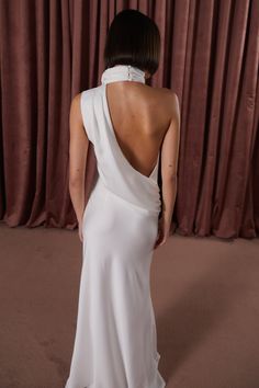 the back of a woman wearing a white dress with a halter neckline and high slit