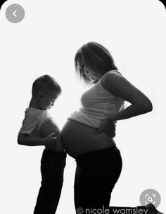 black and white photograph of a pregnant woman holding her baby bumping the belly of a toddler