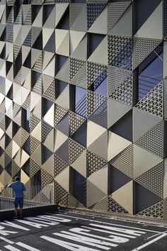 a man walking down a street next to a tall building with geometric designs on it