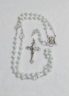 "This rosary is made with white faceted glass beads, clear faceted glass beads, white seed beads, clear seed beads, silver accents, silver medal and silver crucifix What does the rosary symbolize? The rosary is more than a prayer. It symbolizes our destiny in and with God according to Mary's example. To live up to this destiny, we need faith in God's marvelous deeds for us, perseverance in his ways (hope) and a practical attitude toward living our faith, that is charity.  The word rosary itself White Rosary, Cheap Elegant Silver Rosary Bracelet, White Cross Rosary For Jewelry Making, White Beaded Cross Jewelry, White Spiritual Rosary Bracelet With Cross, White Cross Jewelry With 8mm Beads, White Beaded Cross Rosary, White Cross Jewelry With Miraculous Medal, White Faceted Beads Rosary Bracelet Gift