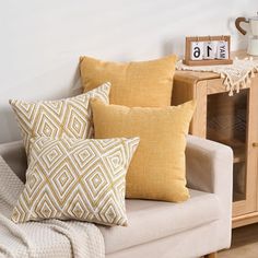 a couch with pillows and a clock on the side table next to it, in front of a white wall