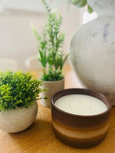 a candle sitting on top of a wooden table next to a pot filled with plants