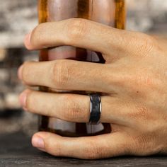 a man's hand with a wedding band holding onto a beer bottle in front of him