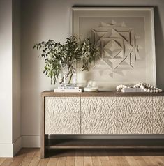 a white cabinet with some plants on top of it next to a wall mounted art piece