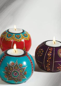 three colorful candles sitting next to each other on top of a white surface with one lit candle in the middle