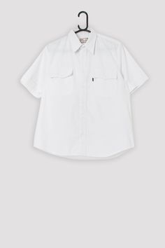 Vintage Levis Sta-Prest shirt in white. This 90s (1999) white Sta-Prest Levis shirt features a white button closure, two chest pockets with white button closures, and a black Levis tab on the left chest pocket.  Made from a mid-weight cotton blend.   Our recommended size: Medium Label says: Medium Condition: Very good Material: 60% cotton, 40% polyester Measurements in inches, laid flat: Pit to pit: 22.5 Shoulders: 17 Front length: 27 Back length: 28 Sleeve length: 10 We recommend that you compa Classic Shirt With Buttons For Streetwear, White Camp Shirt With Button Closure And Relaxed Fit, White Relaxed Fit Camp Shirt With Button Closure, White Button-up Camp Shirt With Placket, White Casual Camp Shirt With Pockets, White Short Sleeve Work Shirt With Pockets, Classic Button-up Streetwear Tops, White Camp Shirt With Spread Collar And Button Closure, Classic Button-up Tops For Streetwear