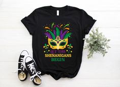 a t - shirt that says let the shennangans begin with a mardi gras mask