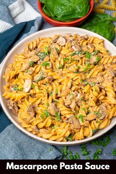 pasta with mushrooms and spinach in a white bowl on a blue cloth next to basil leaves