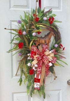 a christmas wreath hanging on the front door with deer head and red ribbon tied around it