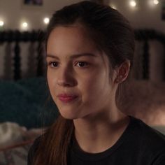 a young woman with long hair looking at the camera while sitting on a bed in a bedroom