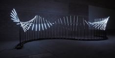 an art installation with white lights on the wall and black iron fence in front of it