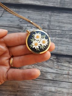 a hand holding a black and white necklace with daisies on the inside of it