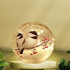 two birds are sitting on a branch in a glass ball with red berries around it